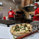 Two pizzaiolos prepare a pie for delivery